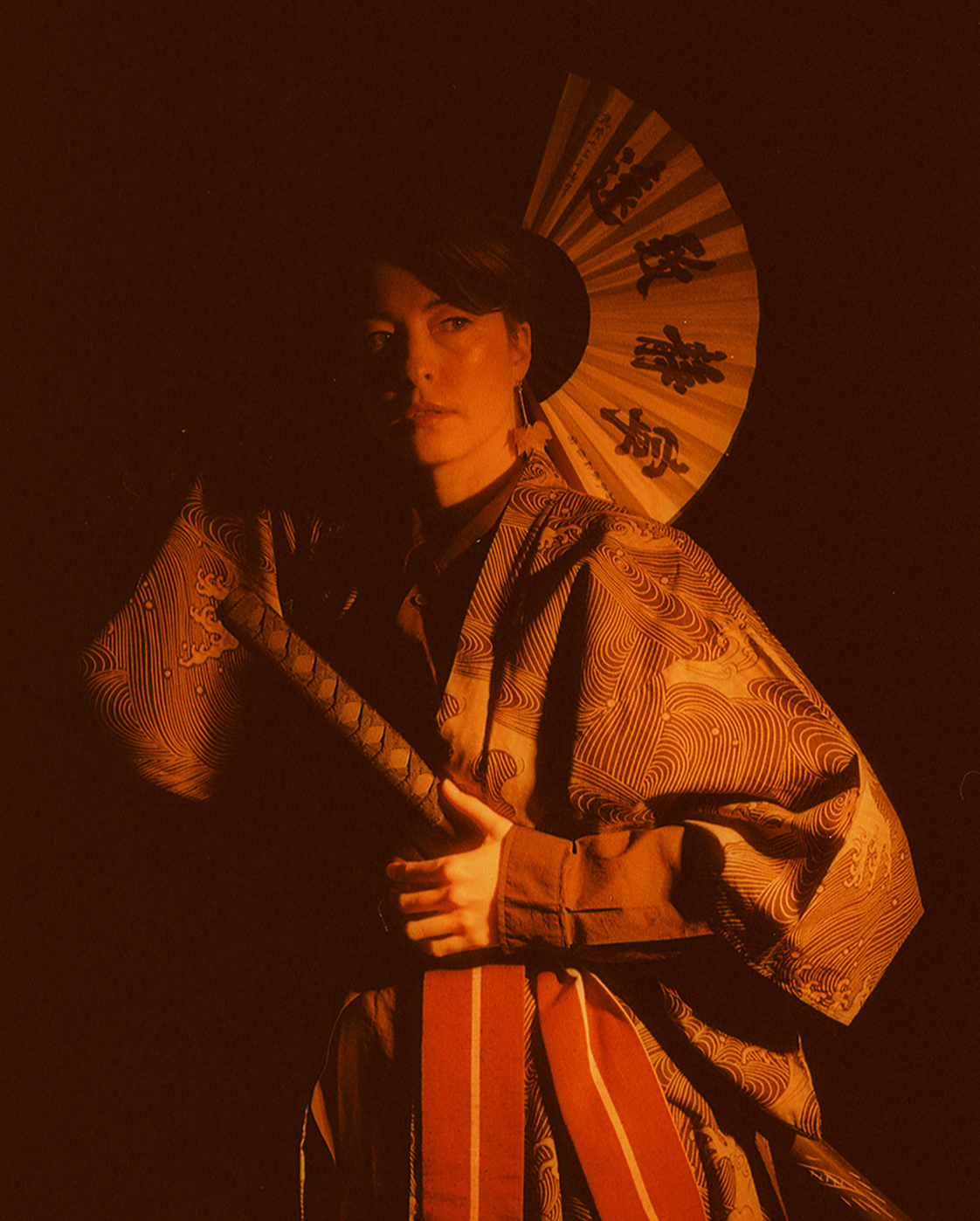 Yulia behind the open fan, all in ember orange